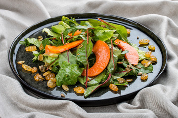 Salad with pumpkin, seeds and raisins on a black plate. Italian cuisine.