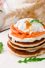 Beautiful pancakes with salmon, poached egg and arugula on a white plate on a light background, decorated with pink roses. Close-up. Space