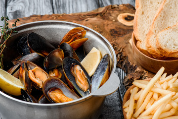 Mussel shells in a gray cauldron in tomato sauce, french fries and croutons on a gray background. Close up. Space