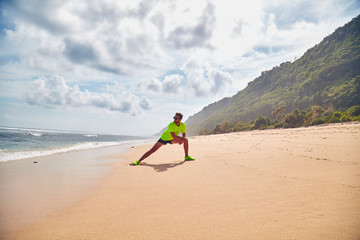 Sportsman stretching on a tropical sandy beach.
