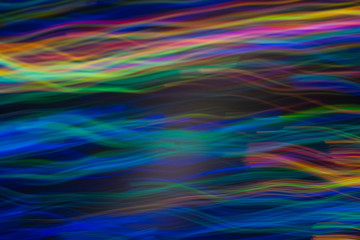 Blurry horizontal wavy lines. Multicolor neon lights in motion on dark background. Bokeh lens flare glow.