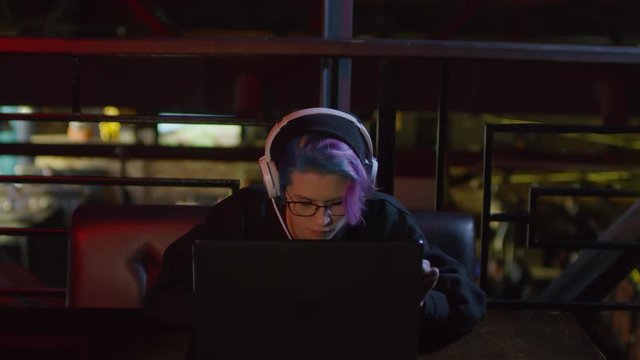 Sequence of videos with young hipster-woman in hoodie and headphones sitting at bar table at laptop, coding and listening to music