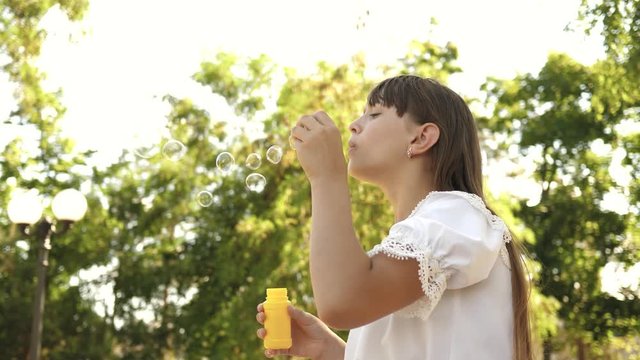 Beautiful girl blowing soap bubbles in the park in spring, summer and smiling. Slow motion. young girl playing in park.