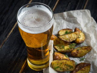 A glass of cold light beer on a wooden table and fries by country