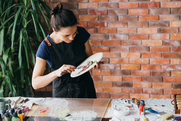Fototapeta premium Clay art. Ceramic craft. Artist studio workplace. Woman with modeling tools creating flower artwork.