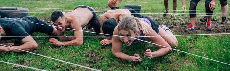 Group of participants in an obstacle course crawling under electrified cables