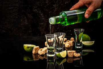 Bottle of absinthe and glasses with burning cube brown sugar on dark background. free space for text. the concept of elite alcohol