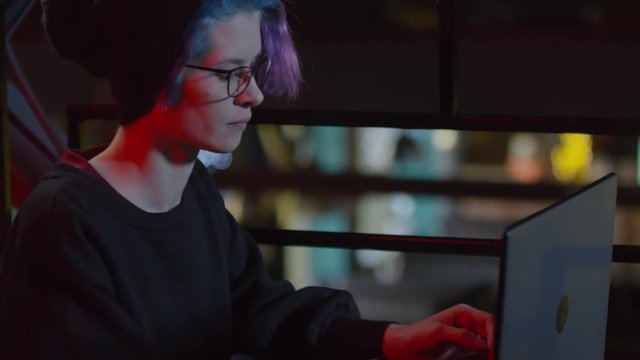Tilt down of young woman-hipster sitting at table in restaurant and typing on laptop keyboard