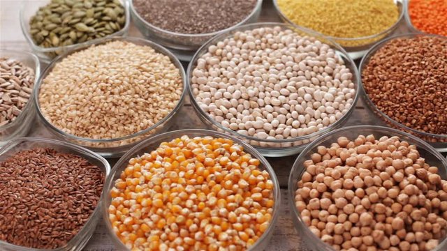 Various seeds and grains on old wooden table, healthy diverse diet concept, top view, camera slide