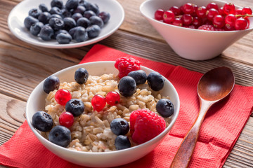 Close up view of porridge with blueberries and raspberries and grain bread on wooden background. Healthy vegan breakfast.