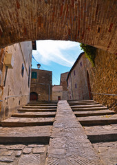 The narrow stone street with steps and arch in the historical center of Castiglione della Pescaia, Grosseto Tuscany, Italy