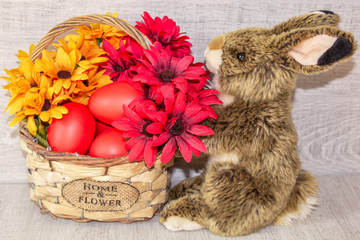 Easter eggs lie in a basket with flowers, on a wooden background, with a fluffy Easter bunny.