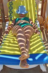 Woman laying on chaise-longue in shadow under beach umbrella enjoying vacation