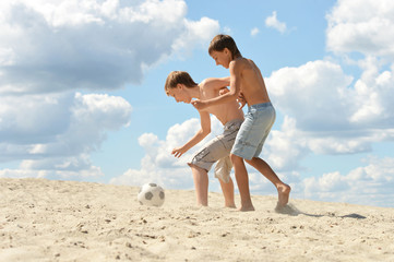 Portrait of two brothers playing football on beach in summer day