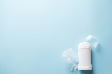 white deodorant or antiperspirant with white feather on blue background for body skin care concept . copy space