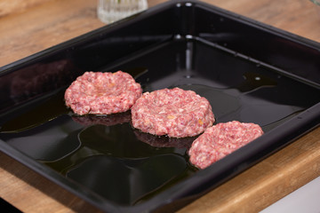 Baking sheet with raw burger patties, closeup