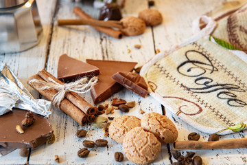 Cinammon sticks tied with jute rope, coffee pot, sweets and cookies on a white wooden background. Coffee break or breakfast backdrop.
