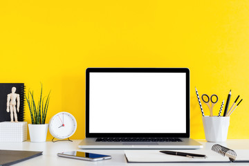 Laptop on desk stationery, succulent, clock and yellow wall for copy space.