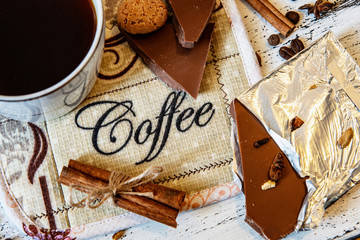 Coffee mug, chocolate, coffee beans, cinnamon sticks and spices on white wooden table. Good morning breakfast or coffee break set background.