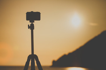 Camera DSLR set on tripod capturing sunset on beach.