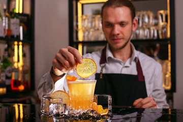 Whiskey Sour alcohol cocktail with orange slice and ice cubes on black mirror background made by man bartender