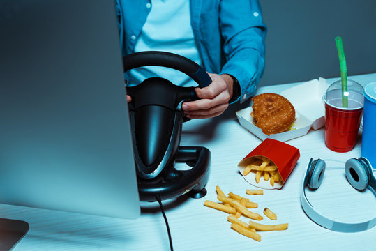 partail view of man holding steering wheel on table with fast food and headphones