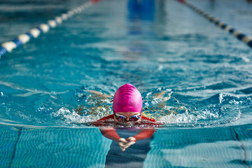 Female athlete in a red-yellow swimsuit is swimming in the style of breaststroke. Splashes of water scatter in different directions.