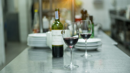 A glass of red wine on top and a bottle of wine behind on the table