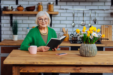 Smiling lady sitting at table and holding open recipe book