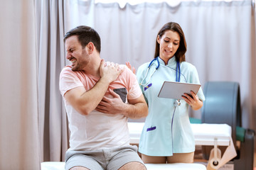 Fototapeta premium Male caucasian patient in pain showing to doctor hurting place. Doctor holding tablet and talking to patient.