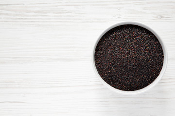 Organic black quinoa in a bowl over white wooden surface, top view. From above, overhead, flat lay. Copy space.