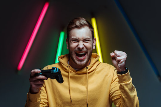 young adult handsome and screaming man looking at camera and holding gamepad