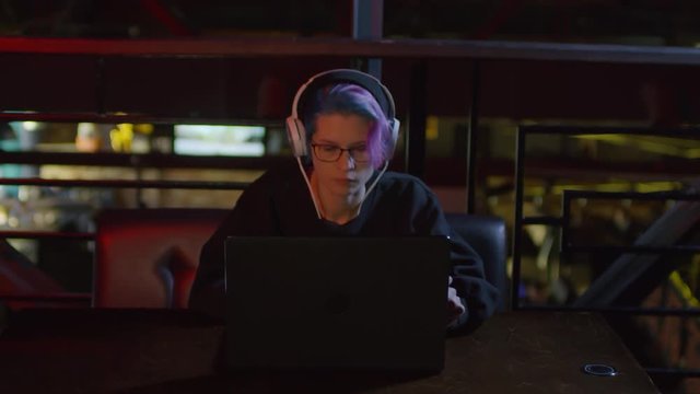 Zoom in of female hipster sitting at laptop in caf&eacute;, listening to music through headphones and programming