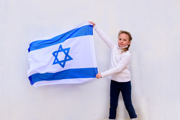 Little patriot jewish girl standing  and enjoying with the flag of Israel on white wall...