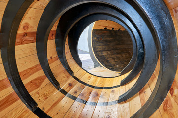 Large, round wooden tube with ribs for children's attraction. The pipe is made of wooden boards and varnished. View from the inside. At the end of the exit pipe.