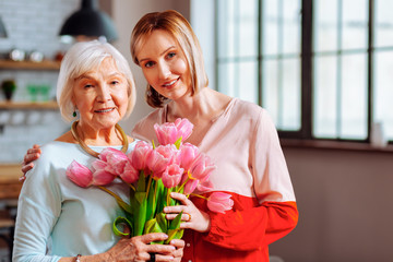 Beautiful mature daughter giving tulips to wrinkled grey-haired mother