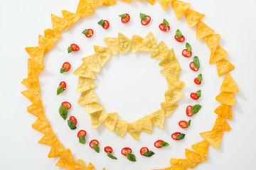 top view of sliced chili peppers and tasty nachos with basil leaves on white background