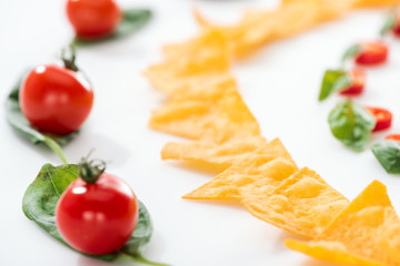 selective focus of tasty nachos and cherry tomatoes with basil on white background