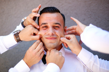 Happy groom posing outdoor,  Groomsmen touches groom's cheeks