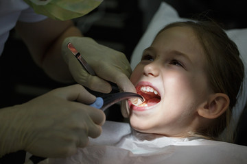 Smiling little girl in the dental office, getting her teeth checked by dentist.