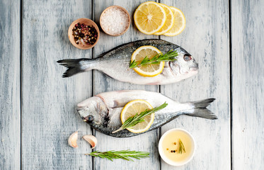 Two fresh raw Dorado fish with spices and olive oil on a wooden table.