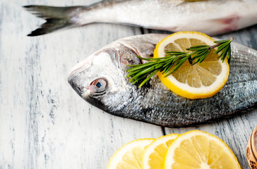 Two fresh raw Dorado fish with spices and olive oil on a wooden table.