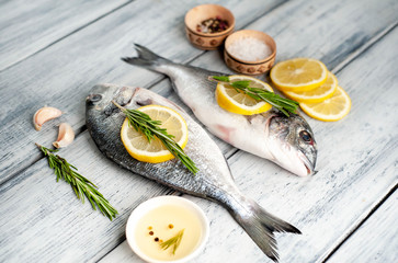 Two fresh raw Dorado fish with spices and olive oil on a wooden table.