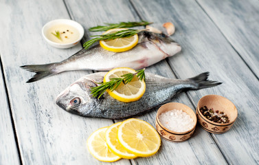 Two fresh raw Dorado fish with spices and olive oil on a wooden table.