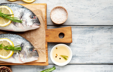  Two fresh raw Dorado fish on a cutting board with spices and olive oil on a wooden table.