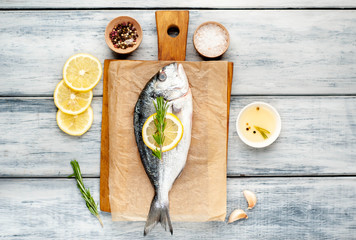 Dorado fish on a cutting board with spices and olive oil on a wooden table. 