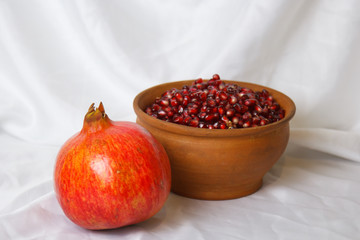 whole ripe pomegranate, pomegranate grains in a brown ceramic plate on a white fabric background,...