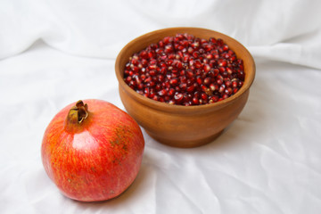 whole ripe pomegranate, pomegranate grains in a brown ceramic plate on a white fabric background, close up