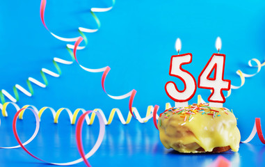 Birthday of fifty four years. Cupcake with white burning candle in the form of number 54. Vivid blue background with copy space