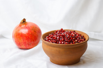 whole ripe pomegranate, pomegranate grains in a brown ceramic plate on a white fabric background, close up